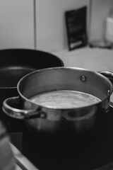 A close-up shot of a hand stirring food in a stainless steel pot on a stovetop, with a blurred background of kitchen ingredients and utensils, capturing a cozy home cooking moment