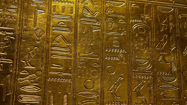 Amazing hieroglyphs carving on golden wall of tomb. Macro view of antique symbols engraved on plate, ancient Egypt.