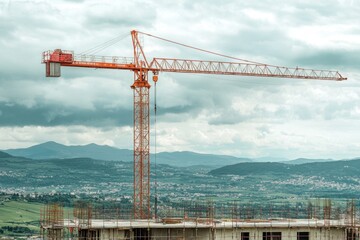 Industrial crane lifting heavy construction materials at a construction site in mountainous area aerial view of urban development with cranes in the background