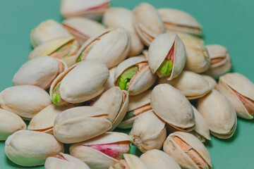 The piled-up nuts are pistachios; the matured nuts are ready to eat. The open-shell nuts have a delicious taste. The pistachio shells are light yellow, with some revealing vibrant green kernels. 