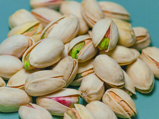 The piled-up nuts are pistachios; the matured nuts are ready to eat. The open-shell nuts have a delicious taste. The pistachio shells are light yellow, with some revealing vibrant green kernels. 