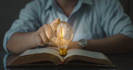 Knowledge and discovery concept. A person holding a light bulb with a glowing light effect over an...