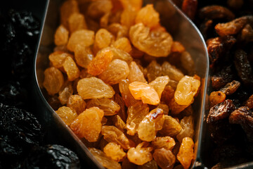 Fresh golden raisins displayed in a metal scoop alongside dried fruits in a market setting