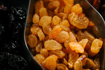 Bright golden raisins in a scooper against a backdrop of dark dried fruits in a market setting