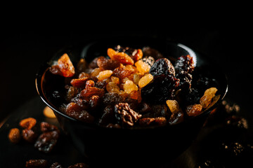 Dried fruits in a black bowl with golden and dark raisins on a dark background