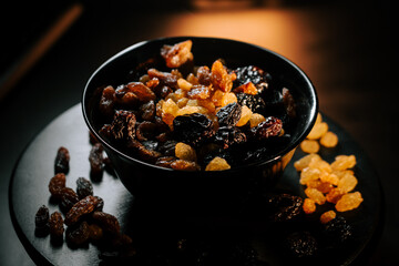 Bowl filled with assorted raisins on a dark wooden table illuminated by soft light
