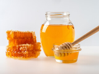 Glass jar full of honey and wooden dipper with honey drop isolated on white background