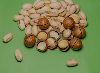On a green background, piles of nutty snacks: macadamias and pistachios. These nuts are ripe, full of flesh and have a delicious flavor. These nuts, rich in protein, unsaturated fats and dietary fiber