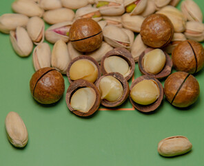 On a green background, piles of nutty snacks: macadamias and pistachios. These nuts are ripe, full of flesh and have a delicious flavor. These nuts, rich in protein, unsaturated fats and dietary fiber