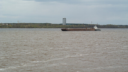 A river tug pushes a large barge moving along the bed of a wide river. Summer navigation on the...