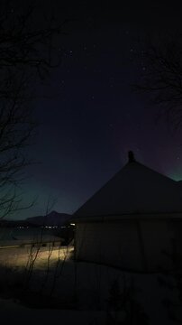 Breathtaking time-lapse of the Aurora Borealis dancing over Lavvu in Northern Norway. The northern lights glow in shades of green, pink, and red. A vertical 4K video