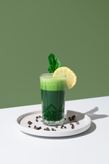 Jugo de espinacas adornado con una rodaja de limón y hoja de espinaca sobre una mesa blanca y...