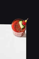 Cóctel Bloody Mary adornado con tomate cherry y pepino sobre fondo negro y blanco