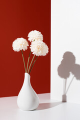 Flores de crisantemo blancas decorativas en un jarrón blanco sobre fondo rojo