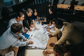Diverse business colleagues gather around a table, actively discussing and strategizing on architectural plans. The mixed group showcases collaborative teamwork and innovative thinking in a