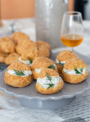 A traditional French savory choux dough cheese puff stuffed with fresh cheese mixed with smoked salmon and dill leaves, glass of cider in background. Pastry well know as specialty of Burgundy 