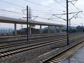 Train Tracks And Elevated Station Platform With Overhead Power Lines Under Clear Sky