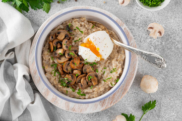 Savory oatmeal porridge for breakfast with poached egg, fried mushrooms and herbs in a bowl on a wooden board. Healthy food. Top view.