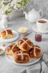 Traditional Easter hot cross buns on a white plate with butter, berry jam and cup of tea. Delicious Easter breakfast.