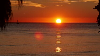 Slow-motion footage of the sun setting over the Mediterranean Sea in Civitavecchia near Rome, Italy. The golden light reflects on the calm water as a sailboat drifts on the horizon.
