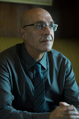 bald Man in Business Attire shirt tie and glasses Reflecting in a Cozy Indoor Setting