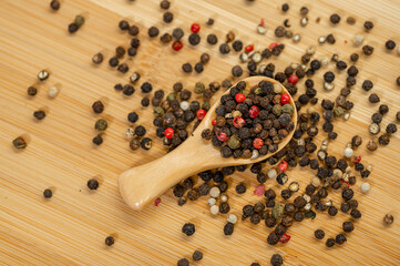 A wooden spoon filled with a mix of black, white, green, and red peppercorns rests on a bamboo...