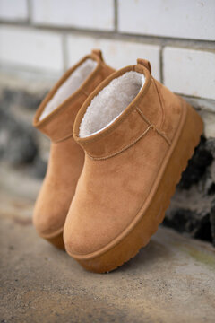 Pair of camel-colored ugg boots with fur inside standing near a white brick wall
