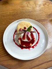 Pancake dessert topped with strawberry jam, whipped cream, and fresh strawberries. Placed on a white ceramic plate, top view, close up