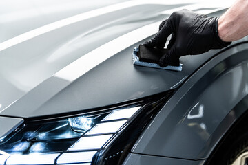 Car wash or detailing studio employee applies ceramic or graphene coating on gray paint for advanced protection and improved shine