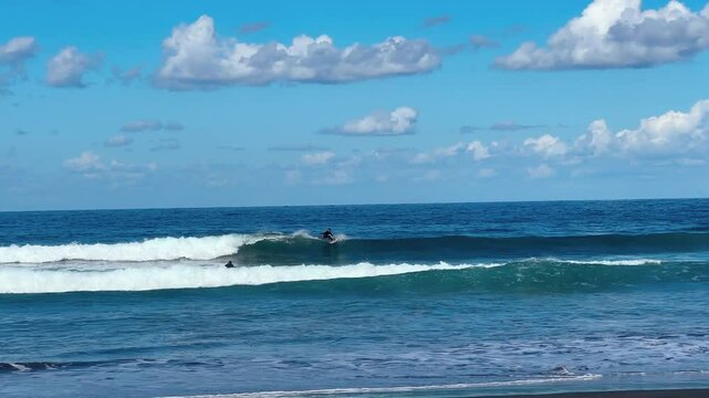 A surfer rides a wave in the Atlantic Ocean at the black volcanic sand beach of Almasiga, Tenerife