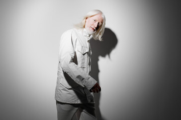 Portrait of an elderly man with long white hair wearing a light outfit, set against a gray background with dramatic shadows highlighting his features, creating a striking visual impact