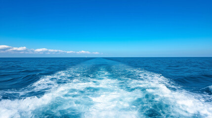 Fototapeta premium Perspective from a sailboat deck showing the wake trailing behind in a vast sea under a clear blue sky with soft white foam creating a sense of adventure and freedom