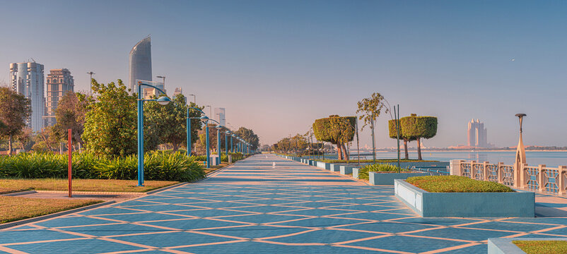 The Abu Dhabi Corniche street at sunrise offers a picturesque view of modern skyscrapers, the calm sea, and a beautifully designed promenade