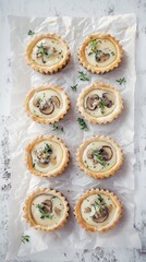 Set of eight mushroom tartlets with flaky crust and creamy filling. Served on parchment paper and white surface. Light ambiance.