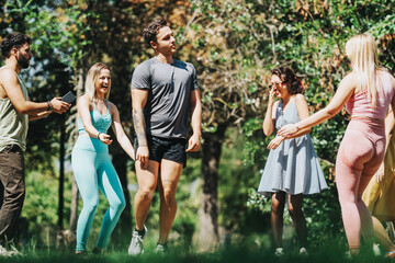 Naklejka premium A group of friends laughing and having fun together in a park setting, dressed in sportswear and summer attire, amidst vibrant greenery on a sunny day.