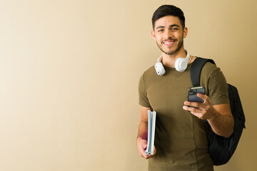 Smiling college student using smartphone and holding books