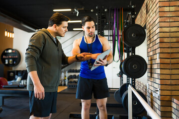 Personal trainer reviewing clipboard while guiding client through exercise routine in contemporary fitness center