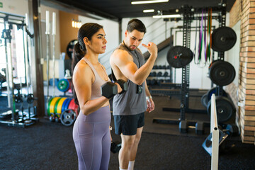 Personal trainer showing young woman how to correctly lift dumbbells during a workout session at...
