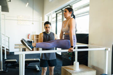 Fototapeta premium Latina fitness enthusiast performing challenging l-sit core workout with trainer guidance during strength training session at gym