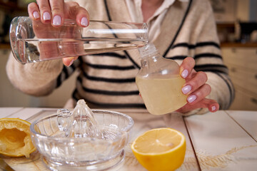Mature woman making her own natural non toxic cleaning products at home with white vinegar and fresh lemon
