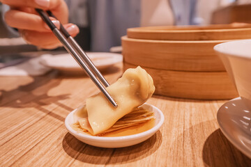 Woman using chopsticks dipping wonton dumpling into soy sauce