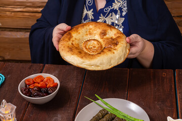 A Muslim woman without a face in a blue hijab and embroidered national dress at a set table
