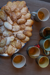 plate of madeleines sprinkled with powdered sugar and cups of tea on the table 