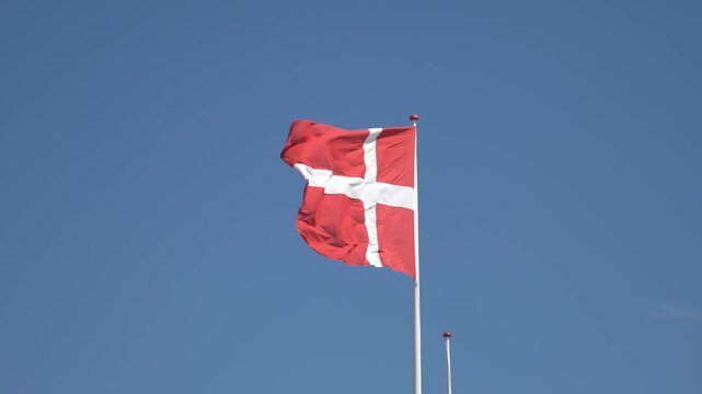 D&auml;nische Flagge weht majest&auml;tisch im Wind vor strahlend blauem Himmel &ndash; Symbol f&uuml;r D&auml;nemark, Freiheit und Nationalstolz in dynamischer Bewegung