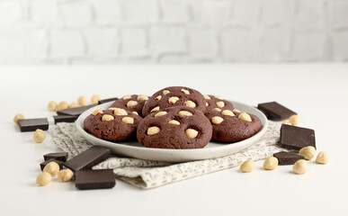Tasty chocolate cookies with hazelnuts on white table, closeup