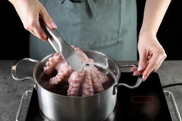 Woman taking boiled octopus from pan on stove, closeup