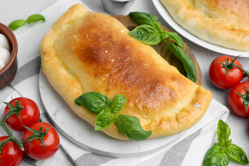 Tasty vegetarian calzone with basil and tomatoes on table, closeup