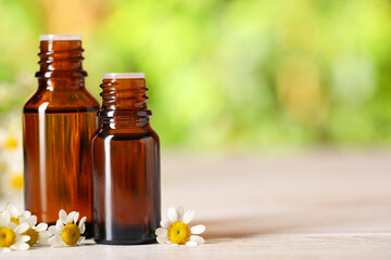 Bottles of essential oil and chamomile flowers on white wooden table against blurred background, closeup. Space for text