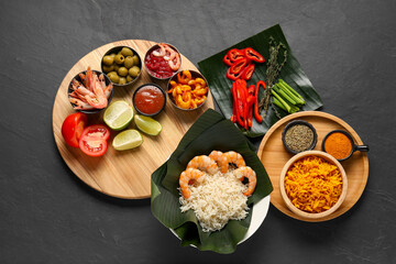 Cut banana leaves with different food, spices and sauce on dark textured table, flat lay. Healthy eco serving