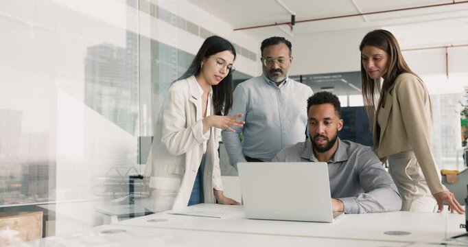 Group of diverse different aged business colleagues watching online product presentation of young African developer, meeting and talking at laptop, discussing Internet marketing concept